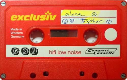 Auto-generated description: A red cassette tape labeled exclusiv features handwritten text with the words alone and together alongside simple smiley and sad face drawings.